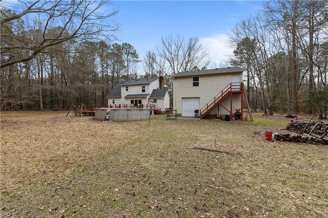 back of house with a garage, an outdoor pool, stairway, and a wooden deck