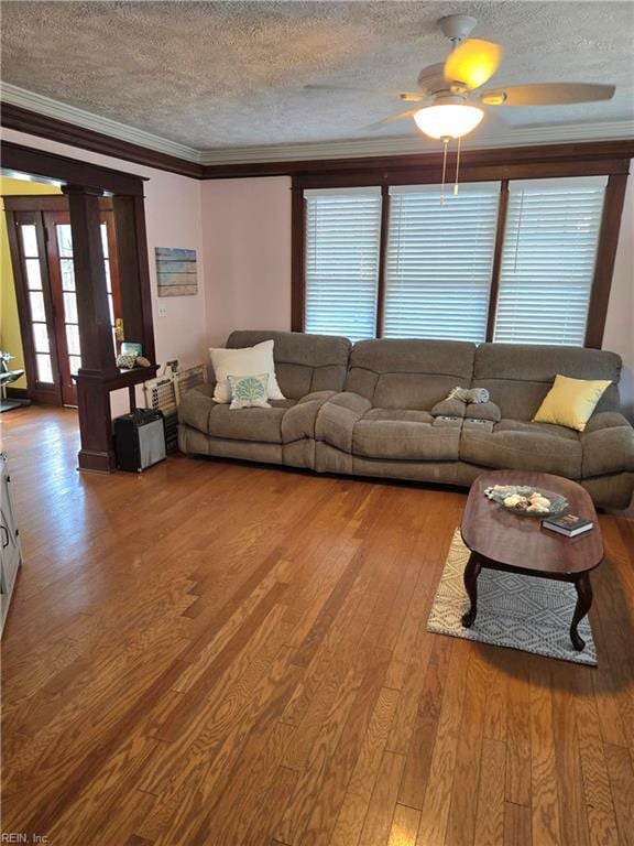 living area featuring plenty of natural light, a textured ceiling, ornamental molding, and wood finished floors