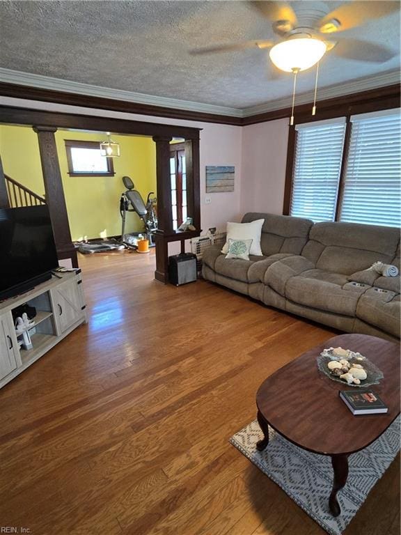 living room with crown molding, decorative columns, ceiling fan, a textured ceiling, and wood finished floors