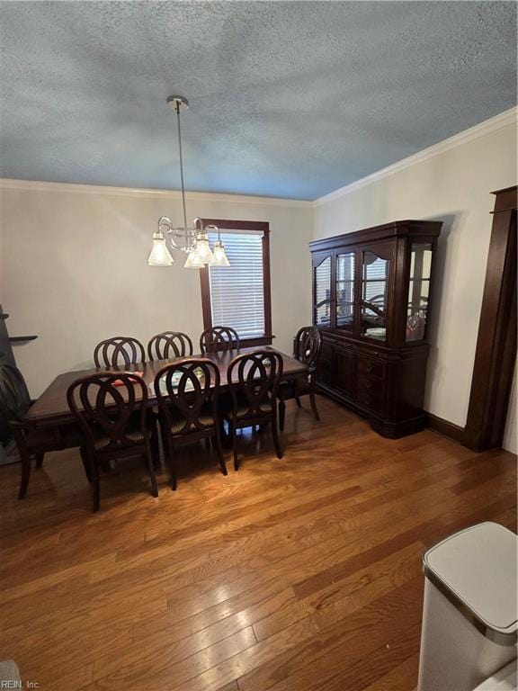 dining room featuring a textured ceiling, wood finished floors, baseboards, ornamental molding, and an inviting chandelier