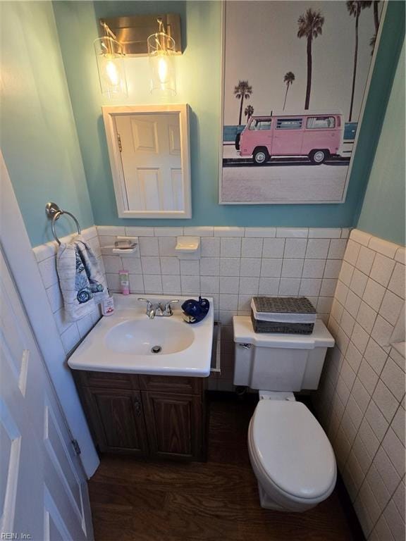 half bathroom featuring toilet, a wainscoted wall, wood finished floors, vanity, and tile walls