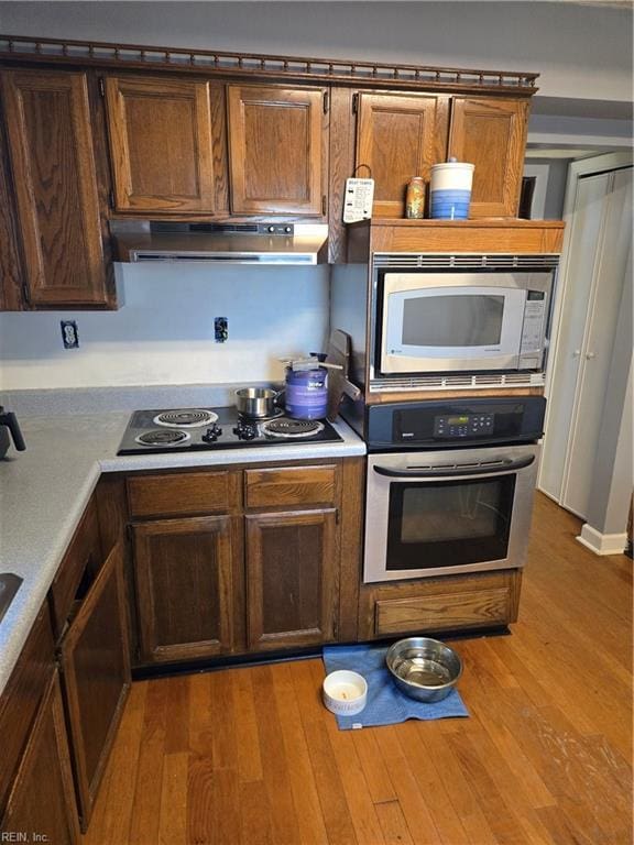 kitchen featuring light wood-type flooring, under cabinet range hood, stainless steel appliances, and light countertops