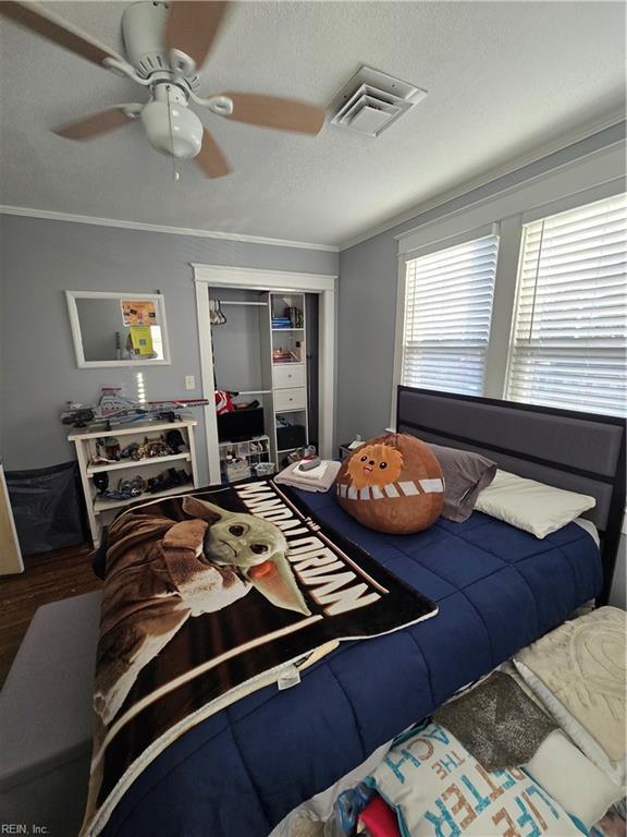 bedroom featuring visible vents, a ceiling fan, wood finished floors, crown molding, and a closet