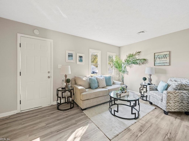 living room featuring light wood-type flooring, visible vents, a textured ceiling, and baseboards