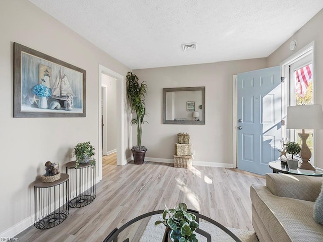 entryway featuring light wood finished floors, baseboards, visible vents, and a textured ceiling