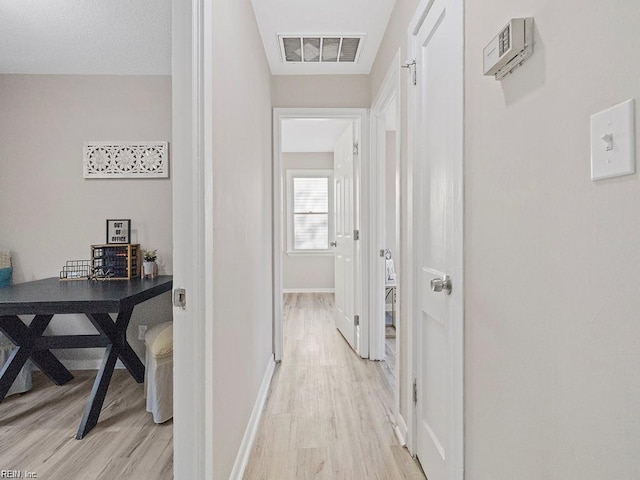 hallway featuring baseboards, visible vents, and light wood finished floors