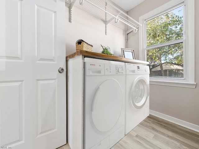 clothes washing area with baseboards, laundry area, light wood-style flooring, and washer and dryer