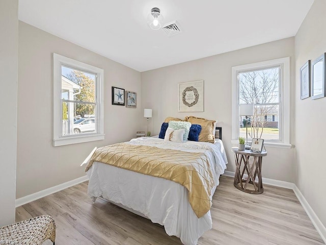 bedroom featuring multiple windows, light wood-style flooring, and baseboards