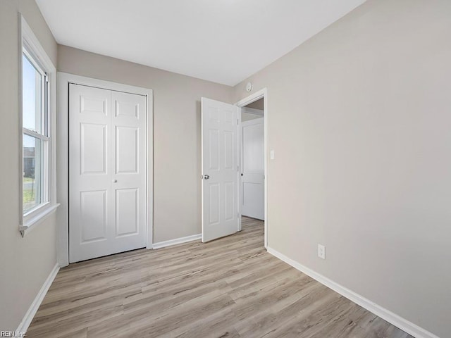 unfurnished bedroom featuring a closet, baseboards, and light wood finished floors