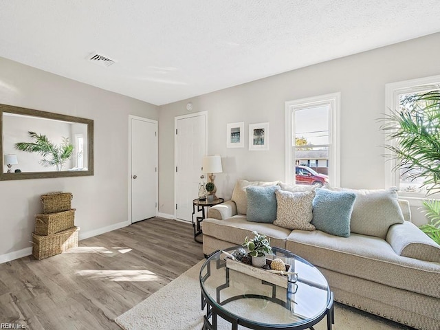 living area with a textured ceiling, wood finished floors, visible vents, and baseboards