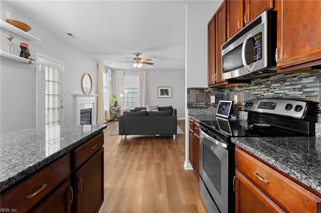 kitchen with tasteful backsplash, open floor plan, dark stone countertops, stainless steel appliances, and light wood-style floors