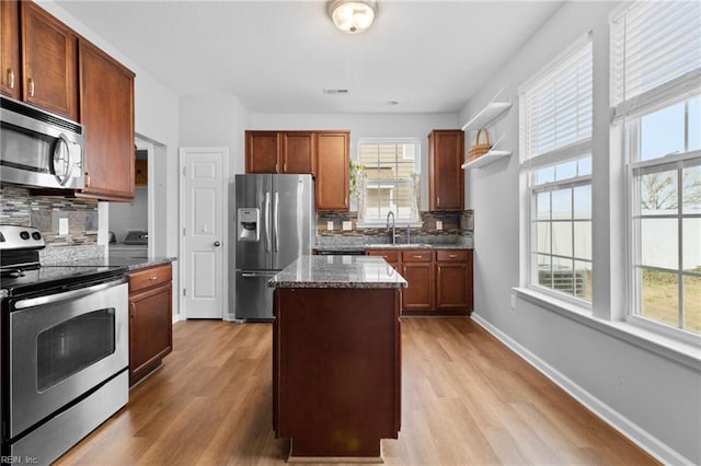 kitchen with light wood finished floors, a kitchen island, appliances with stainless steel finishes, dark stone countertops, and a sink