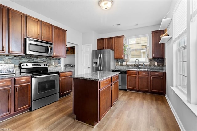 kitchen with a sink, a kitchen island, appliances with stainless steel finishes, dark stone counters, and light wood finished floors