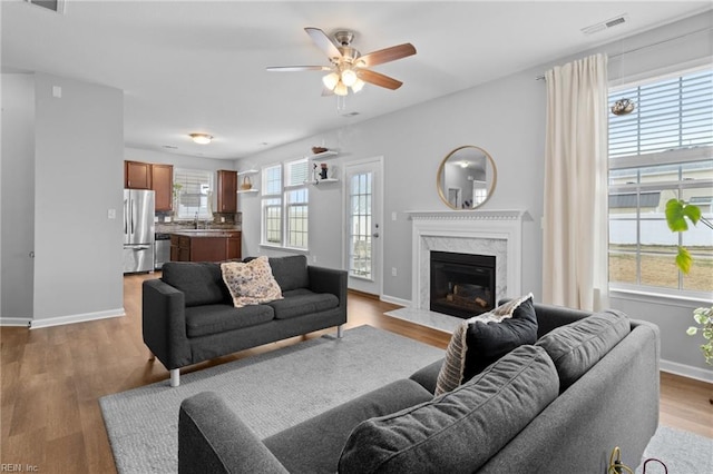 living area featuring light wood-type flooring, a fireplace, visible vents, and baseboards