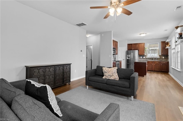 living room with light wood-type flooring, baseboards, visible vents, and ceiling fan