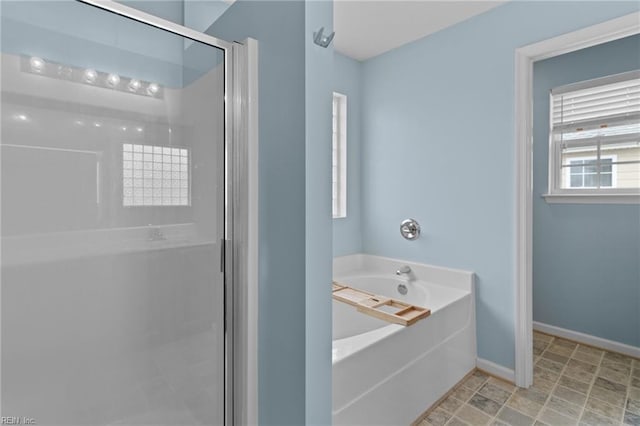 bathroom with a stall shower, a bath, and baseboards