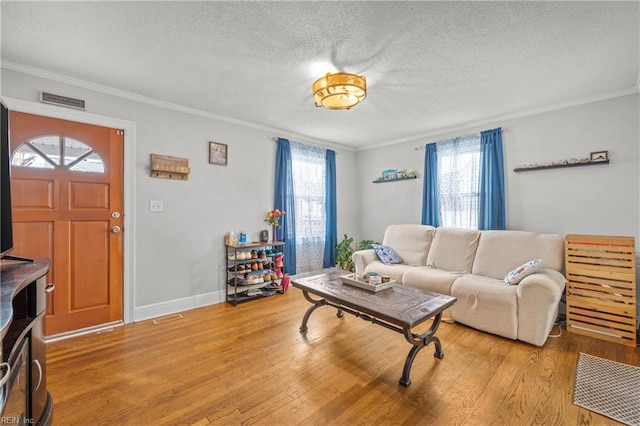 living room featuring light wood-style floors, a textured ceiling, visible vents, and crown molding