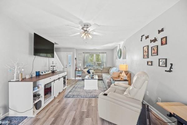 living area with baseboards, a ceiling fan, and light wood-style floors