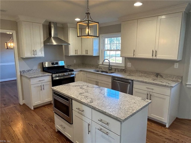 kitchen with white cabinets, appliances with stainless steel finishes, decorative light fixtures, wall chimney range hood, and a sink