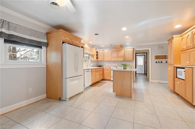 kitchen featuring a center island, light countertops, light brown cabinetry, a healthy amount of sunlight, and white appliances