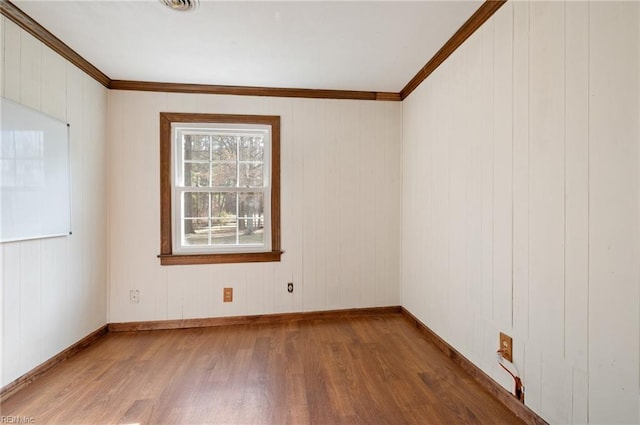 empty room with baseboards, ornamental molding, and wood finished floors