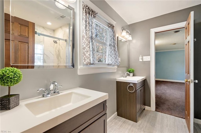 bathroom with a stall shower, two vanities, a sink, and baseboards