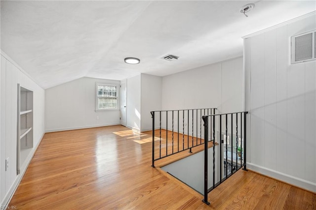 additional living space with built in features, visible vents, vaulted ceiling, and light wood-style flooring