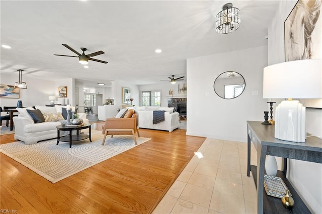 living area featuring a glass covered fireplace, light tile patterned floors, recessed lighting, and ceiling fan with notable chandelier