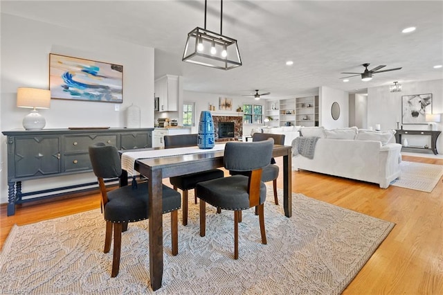 dining room with recessed lighting, a fireplace, a ceiling fan, built in features, and light wood-type flooring