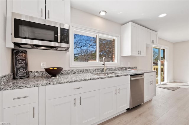 kitchen featuring light stone counters, appliances with stainless steel finishes, white cabinetry, a sink, and light wood-type flooring