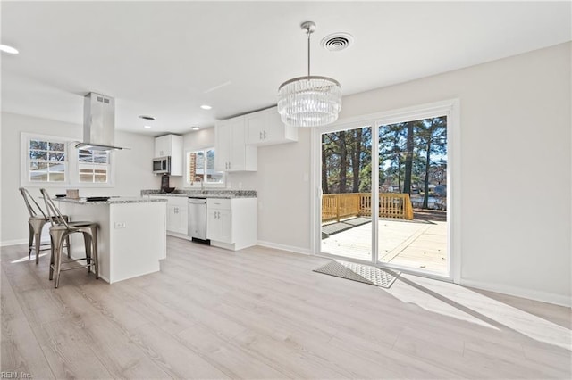 kitchen featuring visible vents, island range hood, white cabinets, hanging light fixtures, and light stone countertops