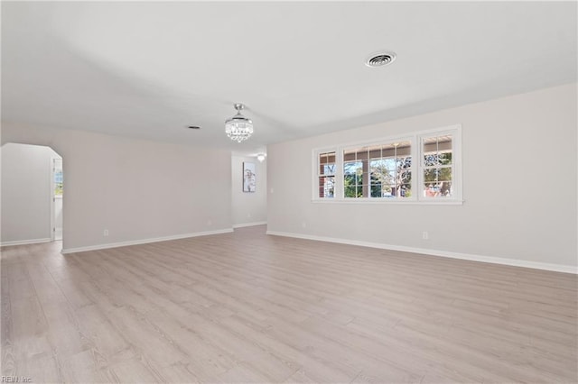 spare room with arched walkways, visible vents, light wood-style flooring, and baseboards