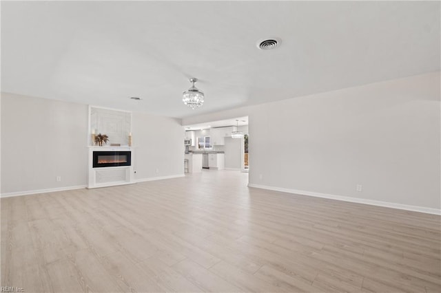 unfurnished living room with light wood-style floors, a glass covered fireplace, visible vents, and baseboards