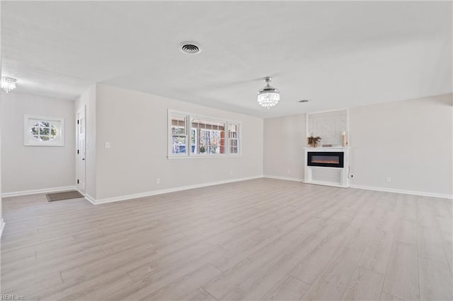 unfurnished living room with baseboards, light wood-type flooring, a glass covered fireplace, and an inviting chandelier