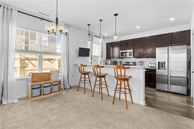 kitchen featuring a breakfast bar area, visible vents, stainless steel appliances, decorative backsplash, and light countertops