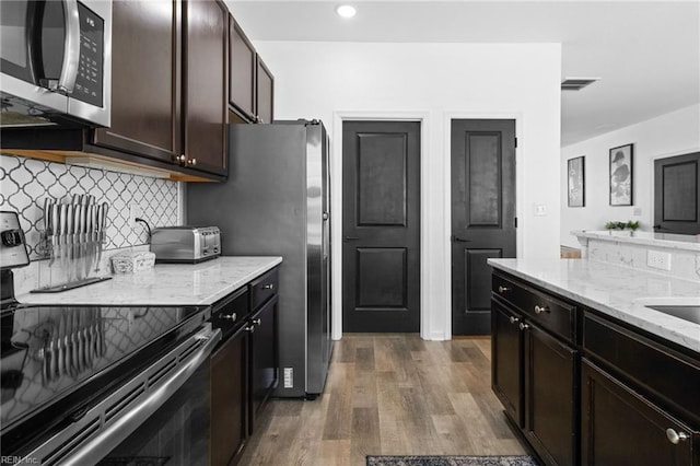 kitchen featuring wood finished floors, light stone countertops, visible vents, stainless steel appliances, and tasteful backsplash