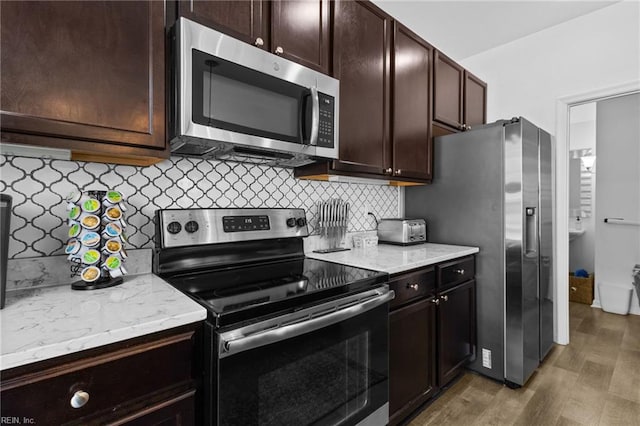 kitchen with light stone counters, backsplash, appliances with stainless steel finishes, and light wood-type flooring