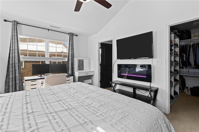 carpeted bedroom featuring a glass covered fireplace, visible vents, lofted ceiling, a closet, and a walk in closet