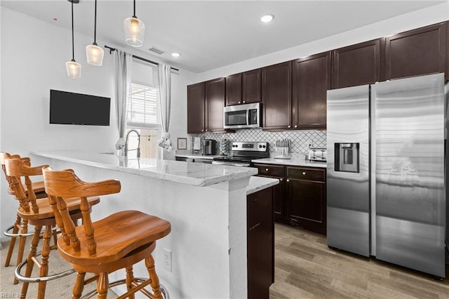 kitchen with decorative backsplash, dark brown cabinets, stainless steel appliances, and light wood-style floors