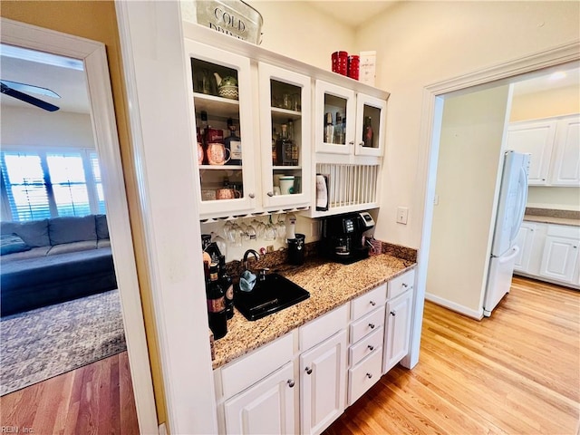 kitchen with light wood-style flooring, glass insert cabinets, light stone counters, freestanding refrigerator, and white cabinetry