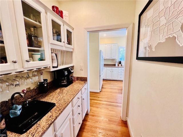 kitchen with light wood finished floors, white cabinets, a sink, and freestanding refrigerator