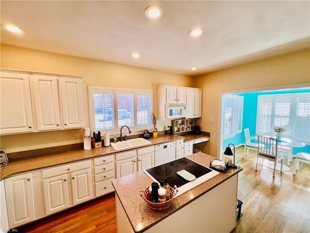 kitchen featuring white appliances, white cabinetry, a sink, and wood finished floors