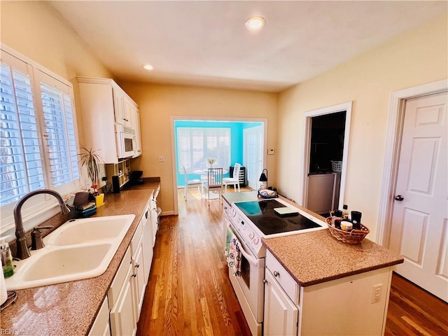 kitchen with white appliances, wood finished floors, a center island, white cabinetry, and a sink