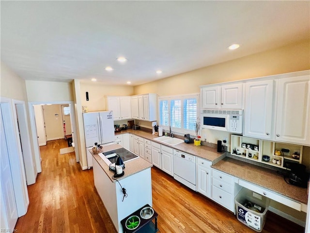 kitchen featuring a center island, light wood finished floors, white cabinetry, a sink, and white appliances