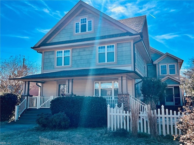 traditional style home featuring a fenced front yard, covered porch, and roof with shingles