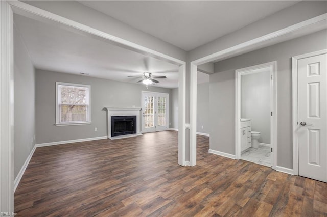 unfurnished living room with dark wood-style floors, plenty of natural light, baseboards, and a fireplace with raised hearth