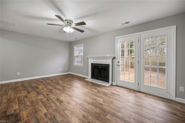 unfurnished living room featuring visible vents, a fireplace with raised hearth, ceiling fan, wood finished floors, and baseboards