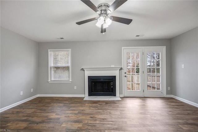 unfurnished living room featuring a fireplace with raised hearth, dark wood-type flooring, visible vents, and baseboards