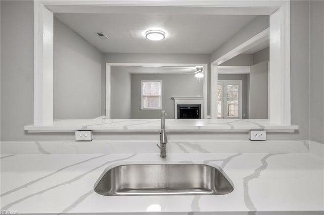 kitchen with a fireplace, a sink, visible vents, and light stone countertops