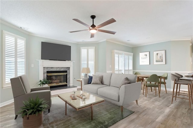 living area with light wood-style floors, a fireplace, visible vents, and crown molding